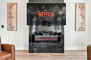Ein modernes Wohnzimmer mit Kamin, einem Wandfernseher und Kunstwerken an den Wänden.