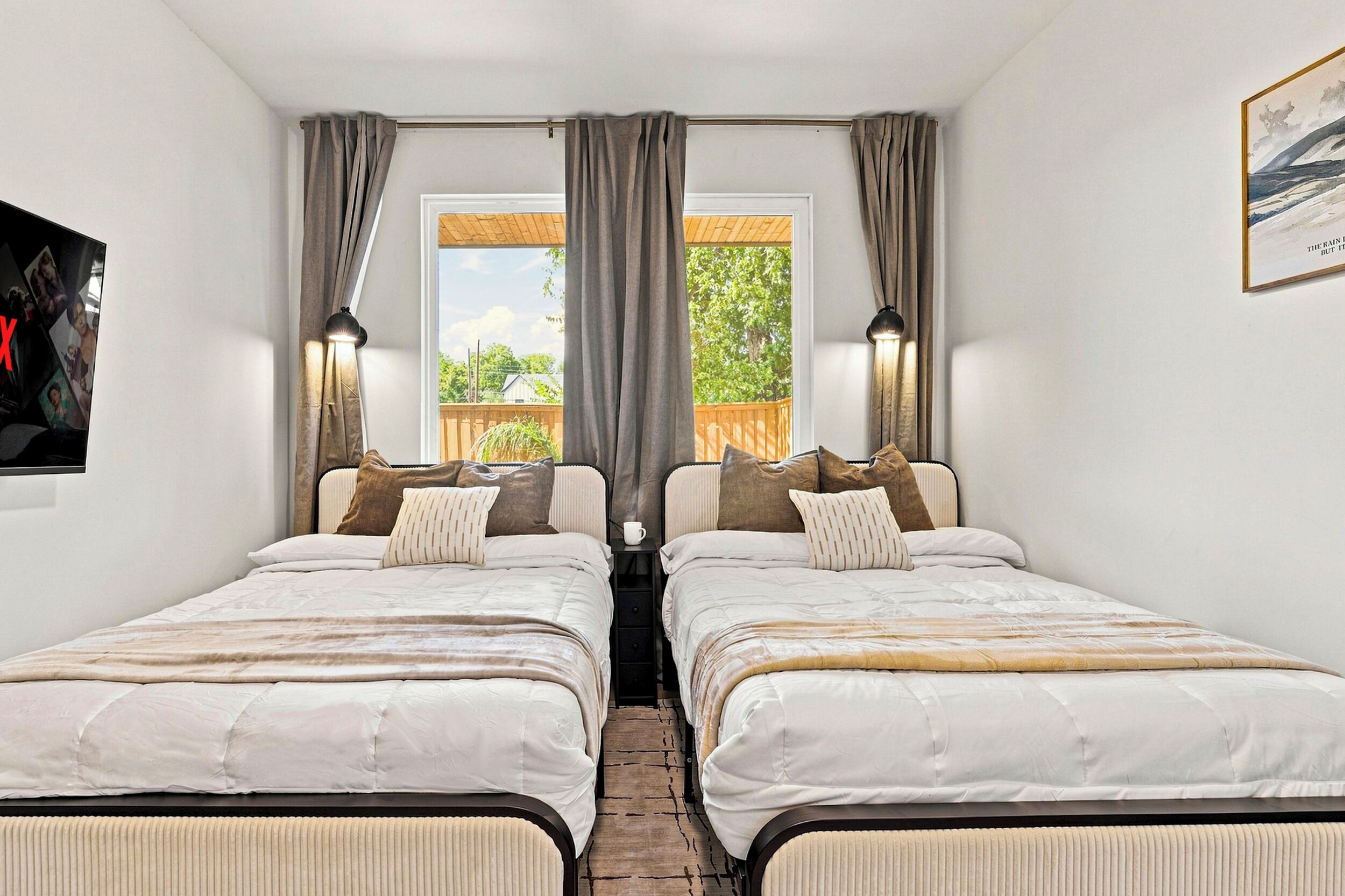 Une chambre double avec deux lits, une fenêtre avec des rideaux, une vue sur la verdure et un tableau au mur.