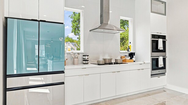 A modern kitchen with white cabinetry, a stainless steel range hood, and a glass refrigerator. - Luxe 6BR Duplex | Rooftop, Hot Tubs, Games & Views (Dallas)