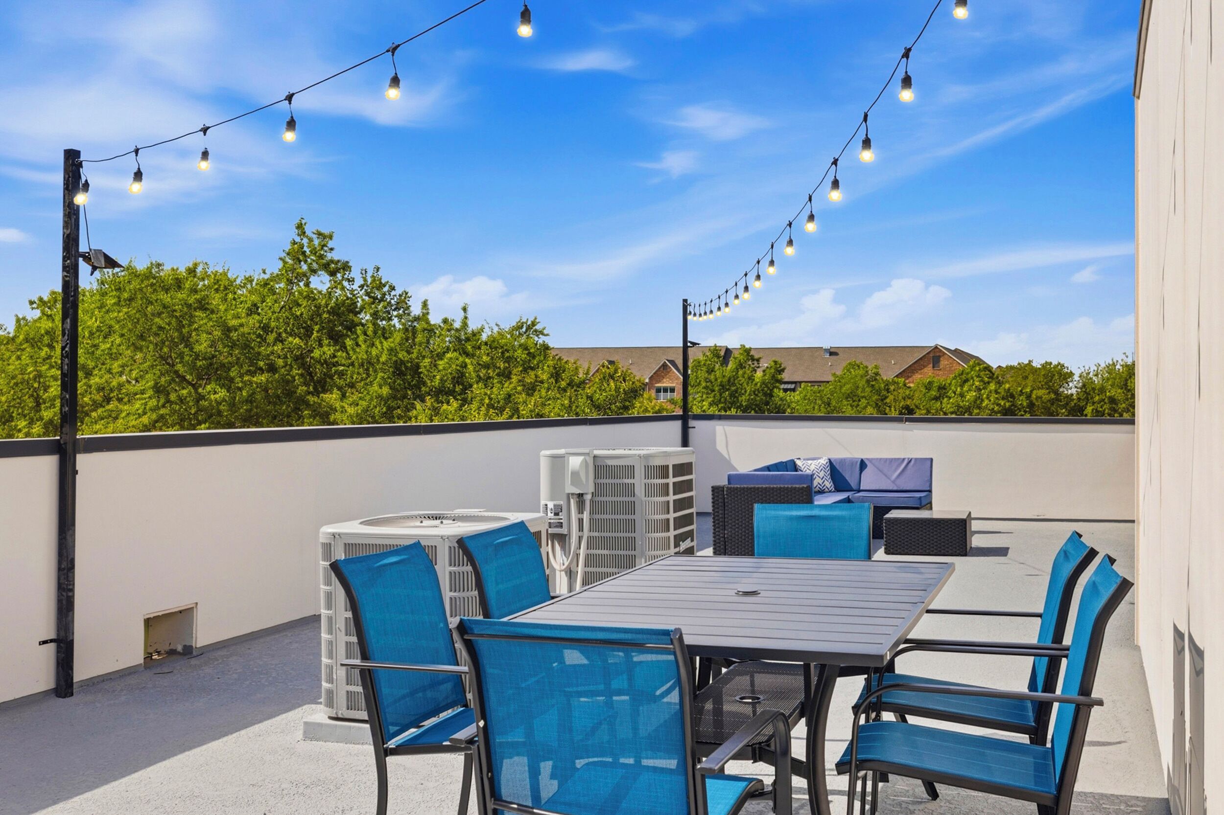 Une terrasse extérieure avec une table et des chaises, des guirlandes lumineuses et des unités de climatisation.