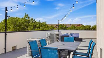 Une terrasse extérieure avec une table et des chaises, des guirlandes lumineuses et des unités de climatisation.