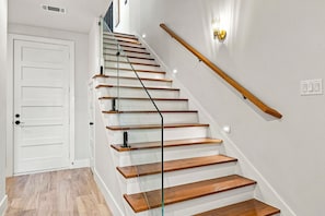 Una escalera de madera con barandilla de vidrio que conduce a una puerta blanca.