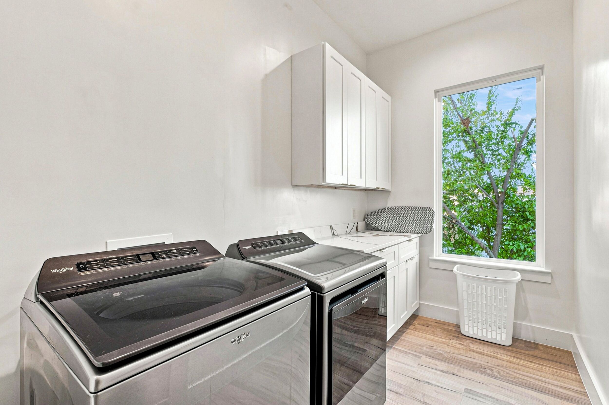 A laundry room with a washer and dryer, a window with a view of trees, and a white cabinet above the counter.