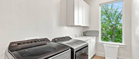 A laundry room with a washer and dryer, a window with a view of trees, and a white cabinet above the counter.