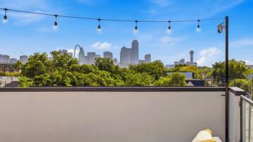 Terraza en la azotea con vistas al horizonte de la ciudad, luces colgantes y una cámara de seguridad.