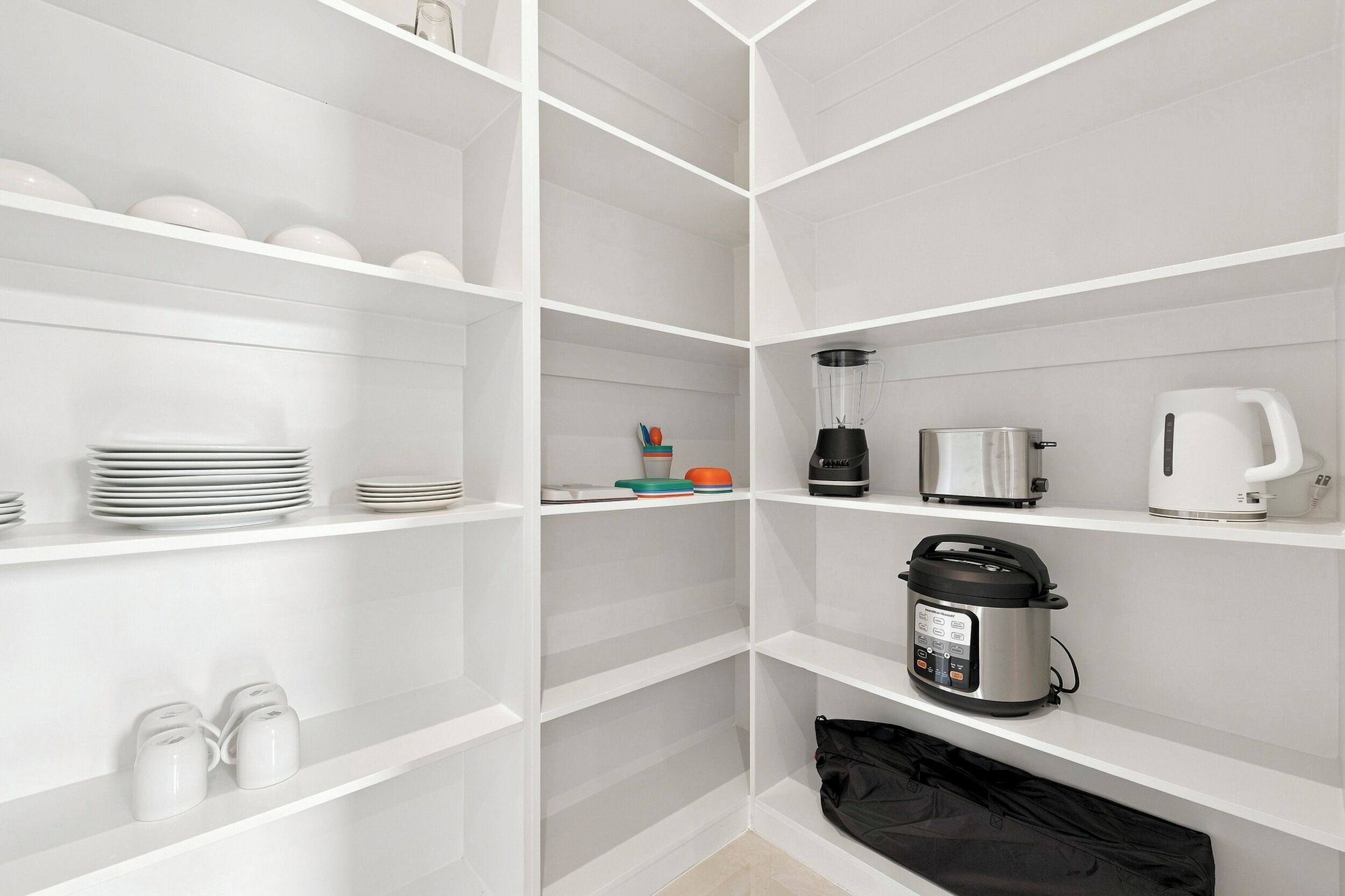 Una cocina moderna con armarios blancos, una cafetera, una licuadora, una cocedora de arroz y una bolsa negra en el estante inferior.