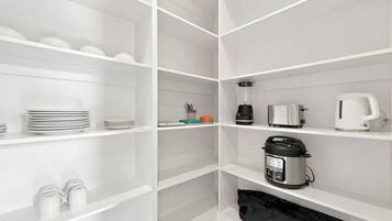 Una cocina moderna con armarios blancos, una cafetera, una licuadora, una cocedora de arroz y una bolsa negra en el estante inferior.