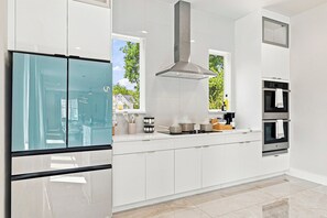A modern kitchen with white cabinetry, a stainless steel range hood, and a glass refrigerator. - Skyline Rooftop & Hot Tub | Near Trinity Groves (Dallas)