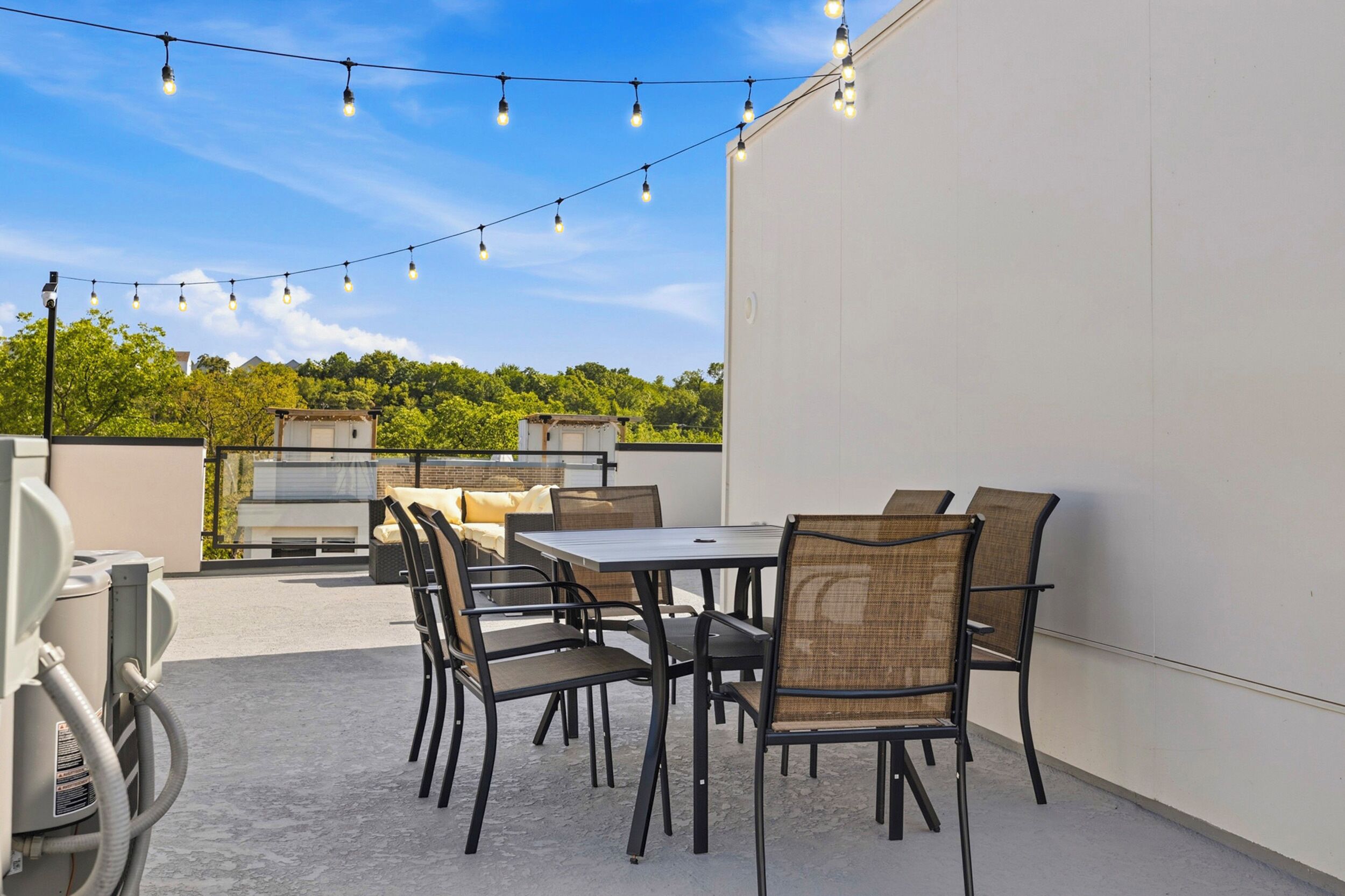 Une terrasse extérieure avec une table et des chaises, des guirlandes lumineuses et une vue sur un bâtiment et des arbres.