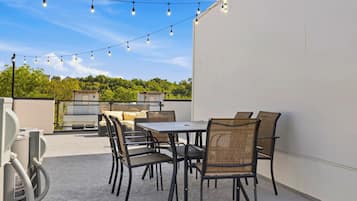 Une terrasse extérieure avec une table et des chaises, des guirlandes lumineuses et une vue sur un bâtiment et des arbres.