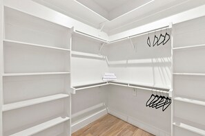 A walk-in closet with white shelving units and hanging space. - Skyline Rooftop & Hot Tub | Near Trinity Groves (Dallas)