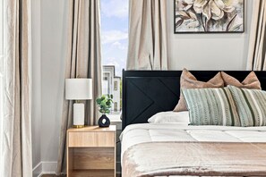 A neatly arranged bedroom with a bed, bedside table, lamp, and a painting on the wall. - Skyline Rooftop & Hot Tub | Near Trinity Groves (Dallas)