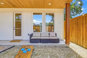 Un patio techado con un sofá de mimbre, una mesa de madera con cojines y una valla de madera.