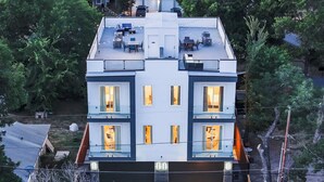 A modern multi-story building with a flat roof, large windows, and a visible outdoor seating area. - Luxe Dallas Home w/ Rooftop, Hot Tub, Yard & Views (Dallas)