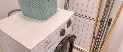A laundry area with a washing machine, a metal drying rack, and a red bucket.