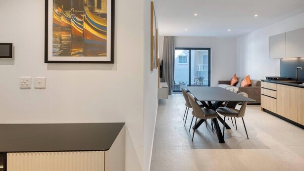 A modern kitchen with a dining area, a large painting on the wall, and a view to the outside. - Designer Msida Suite | W/Balcony & Private Terrace (Msida)