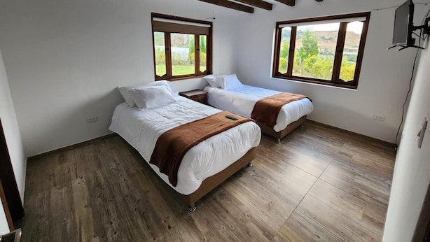 A bedroom with two beds, wooden flooring, and large windows. - Cabin near Villa de Leyva, Sachica, Boy (Sáchica)