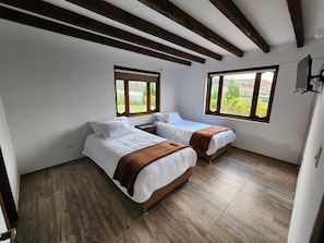 A bedroom with two beds, wooden flooring, and large windows.
