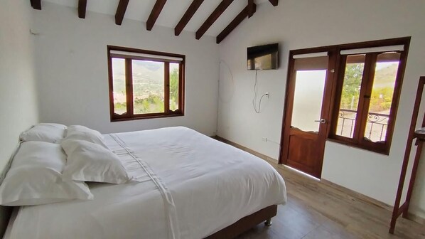 A bedroom with a bed, a TV mounted on the wall, and a balcony door.