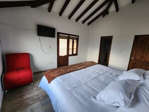 A bedroom with a bed, a red chair, a television, and wooden beams on the ceiling.