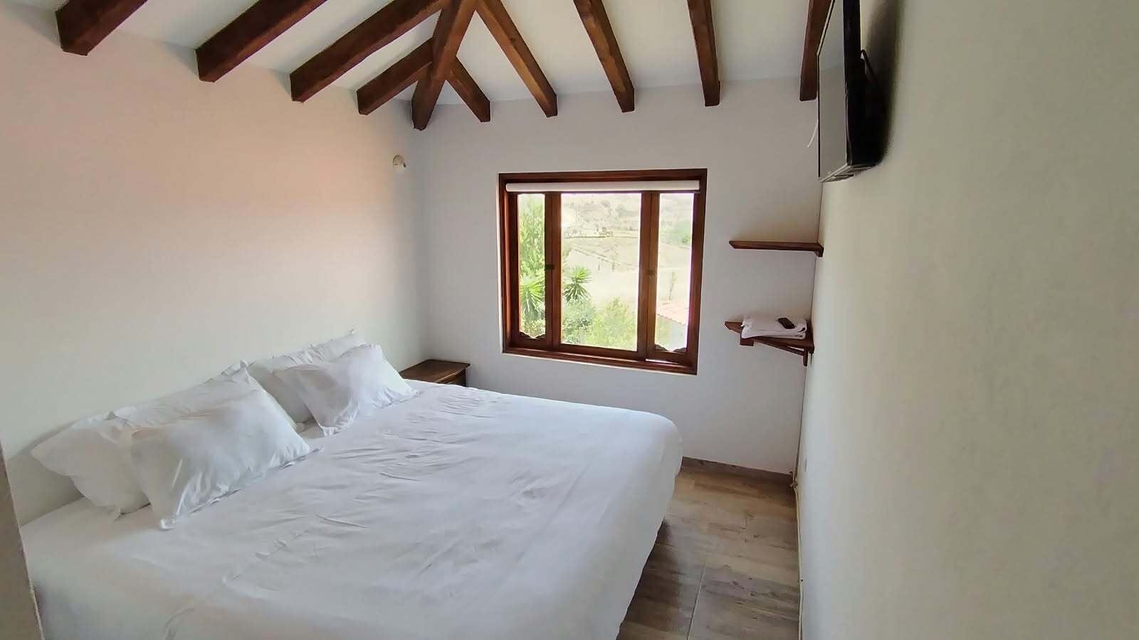 A bedroom with a bed, a window, and wooden beams on the ceiling.