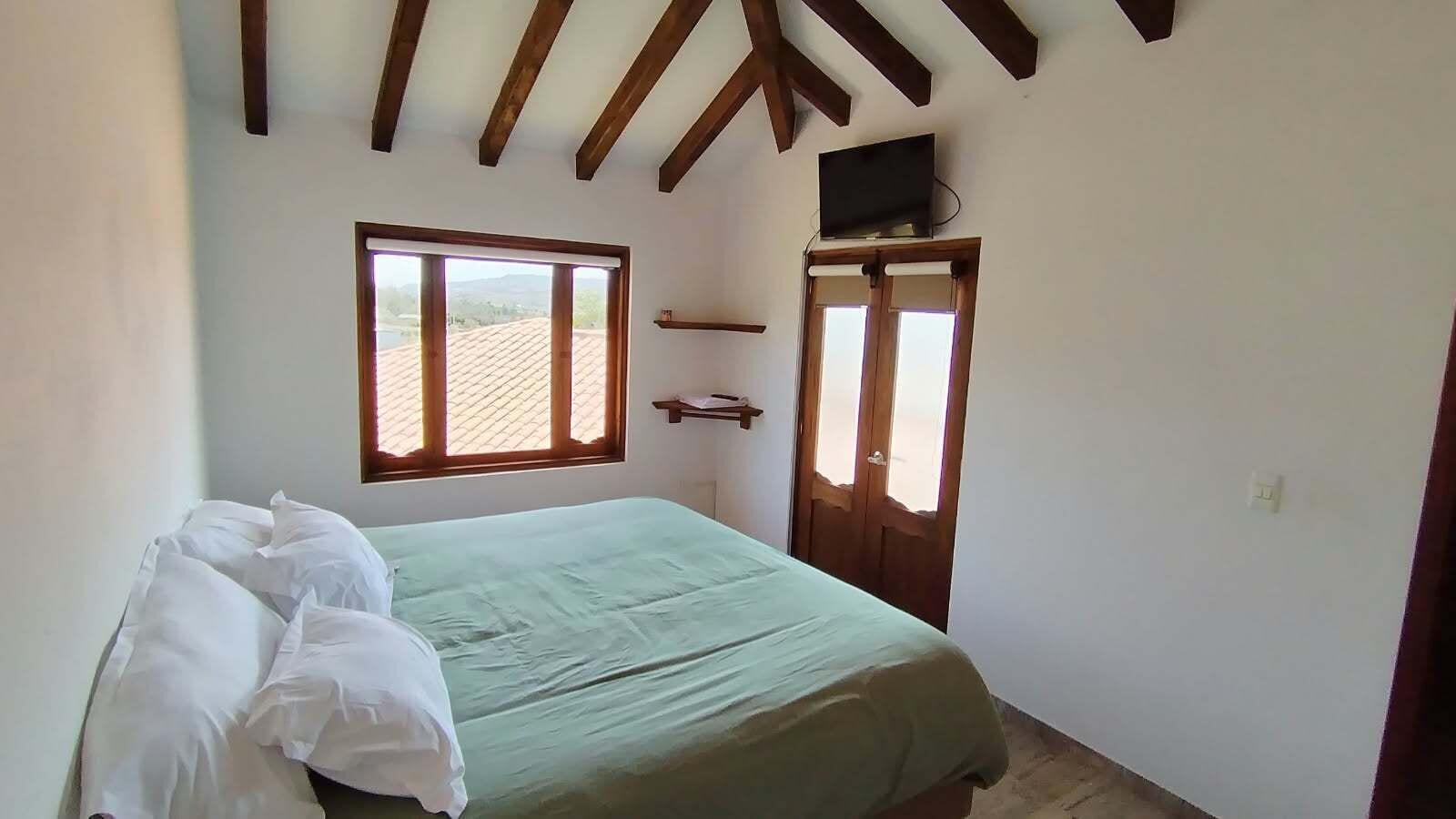 A bedroom with a bed, a window, a door, and a television on the wall.