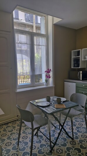 Een eetgedeelte met een tafel voor twee personen, stoelen, een raam met uitzicht en een keuken met apparatuur.