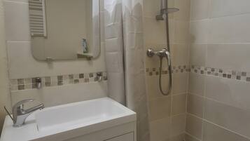 Een badkamer met een douche, een wastafel en een spiegel.