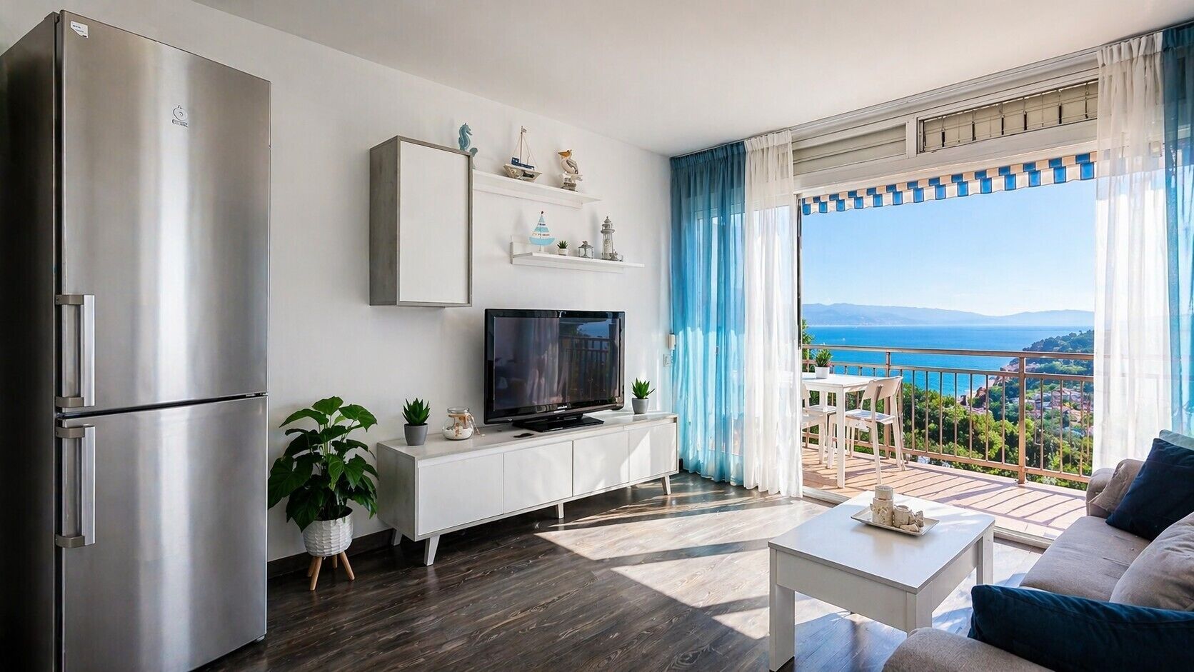 Una sala moderna con un televisor de pantalla plana, un mueble blanco, una zona de comedor con mesa y sillas, y un balcón con vistas.