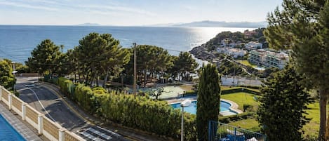 Uma área residencial à beira-mar, com piscina, uma estrada sinuosa e vista para o mar.