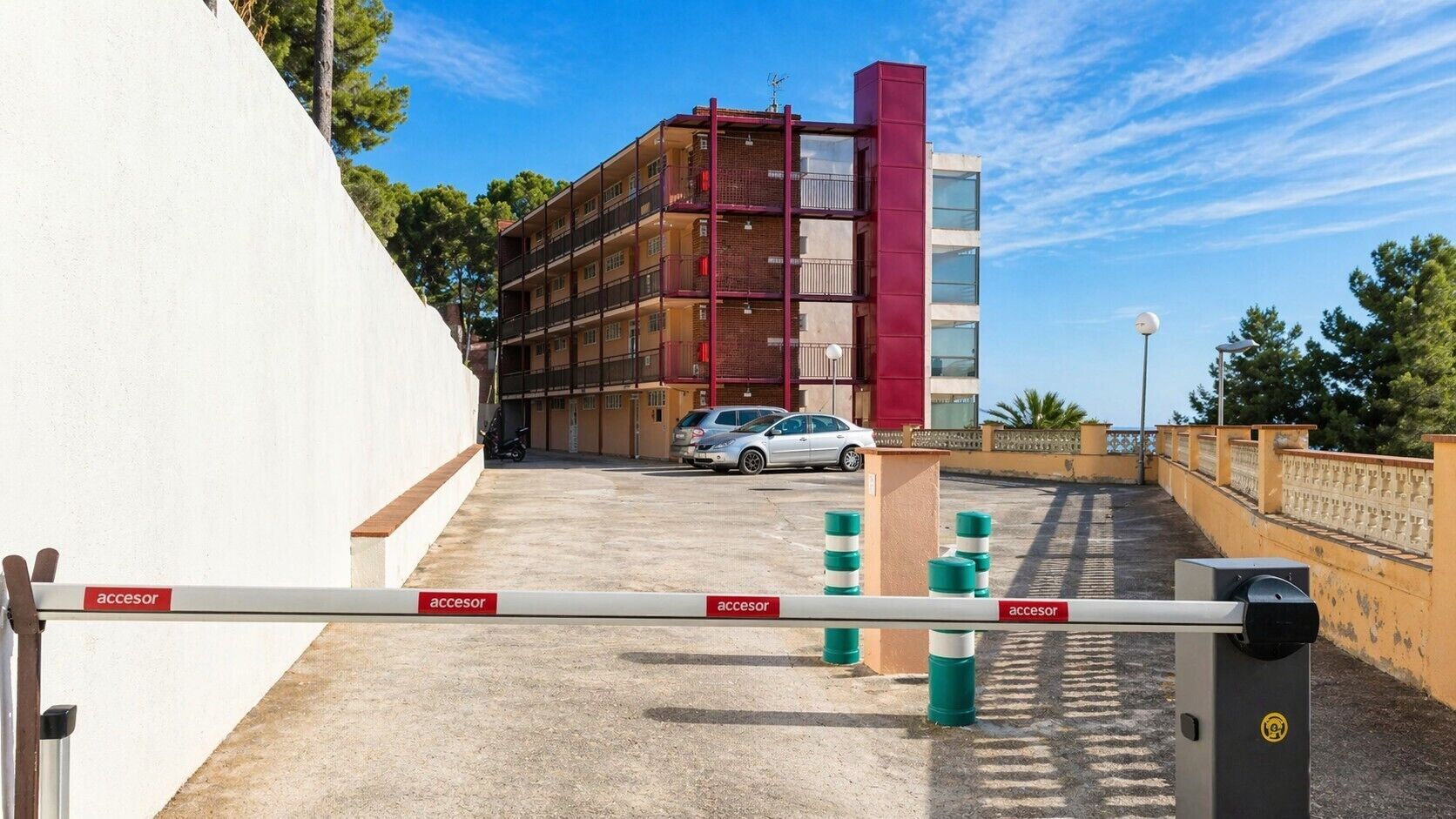 A gated parking area with a red and beige building in the background.