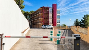 Zona d'aparcament tancada amb un edifici vermell i beix al fons.