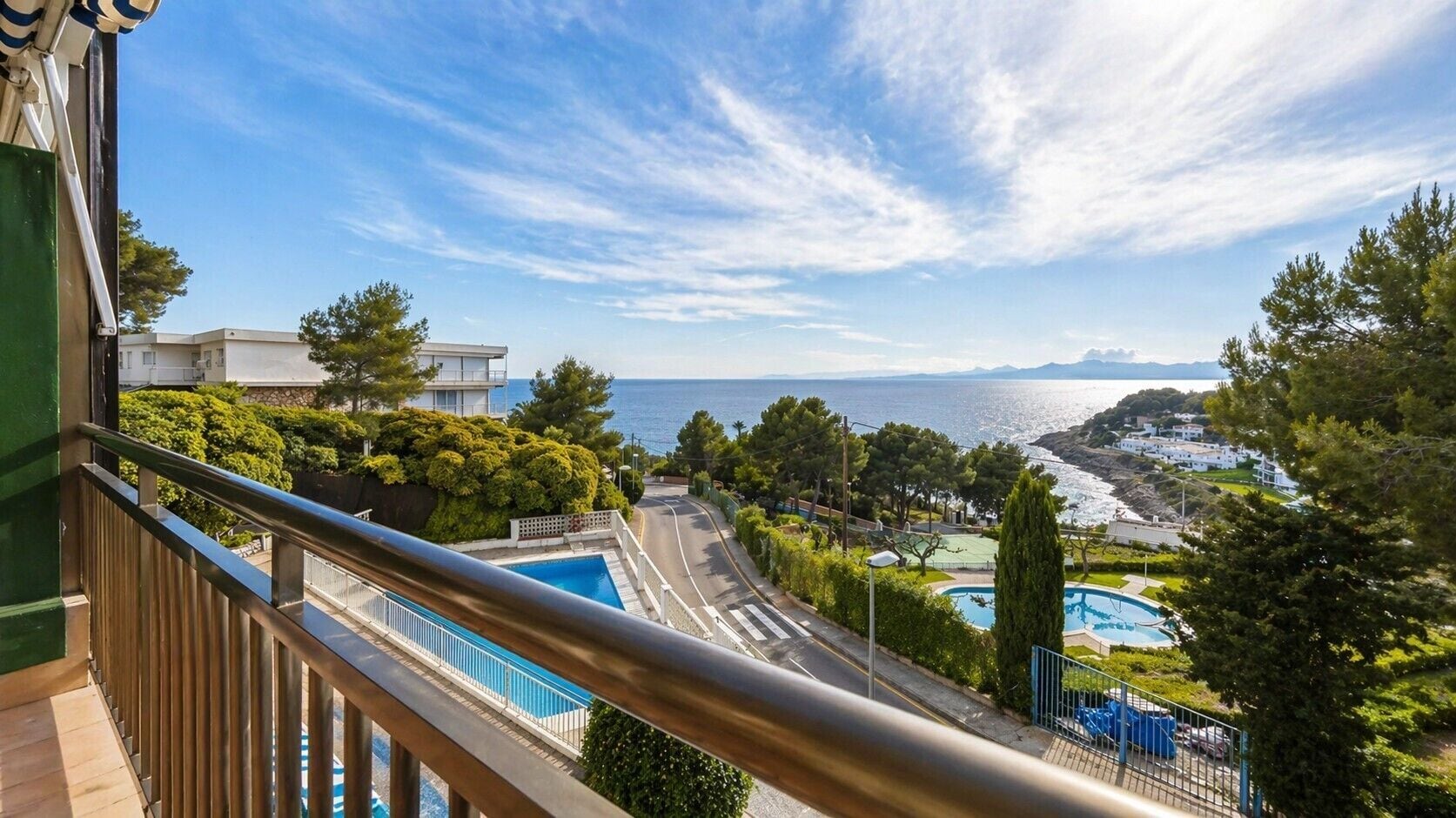 A balcony with a view of a swimming pool, a road, and a coastal landscape.