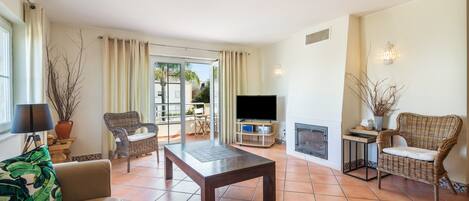 Una sala de estar con televisor, chimenea y balcón con cortinas.