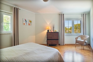 Une chambre à coucher comprenant un lit, une commode, une chaise et une fenêtre donnant sur un paysage verdoyant.
