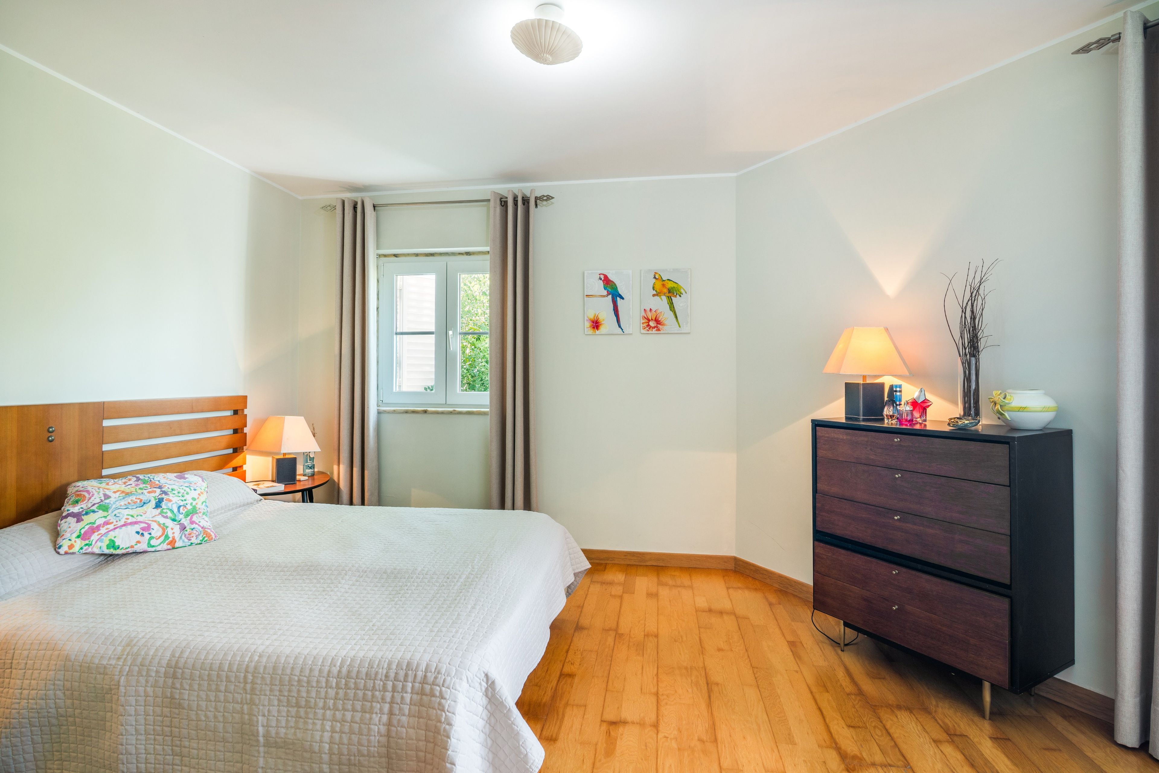 A bedroom with a bed, a dresser, a nightstand, and a window with curtains.