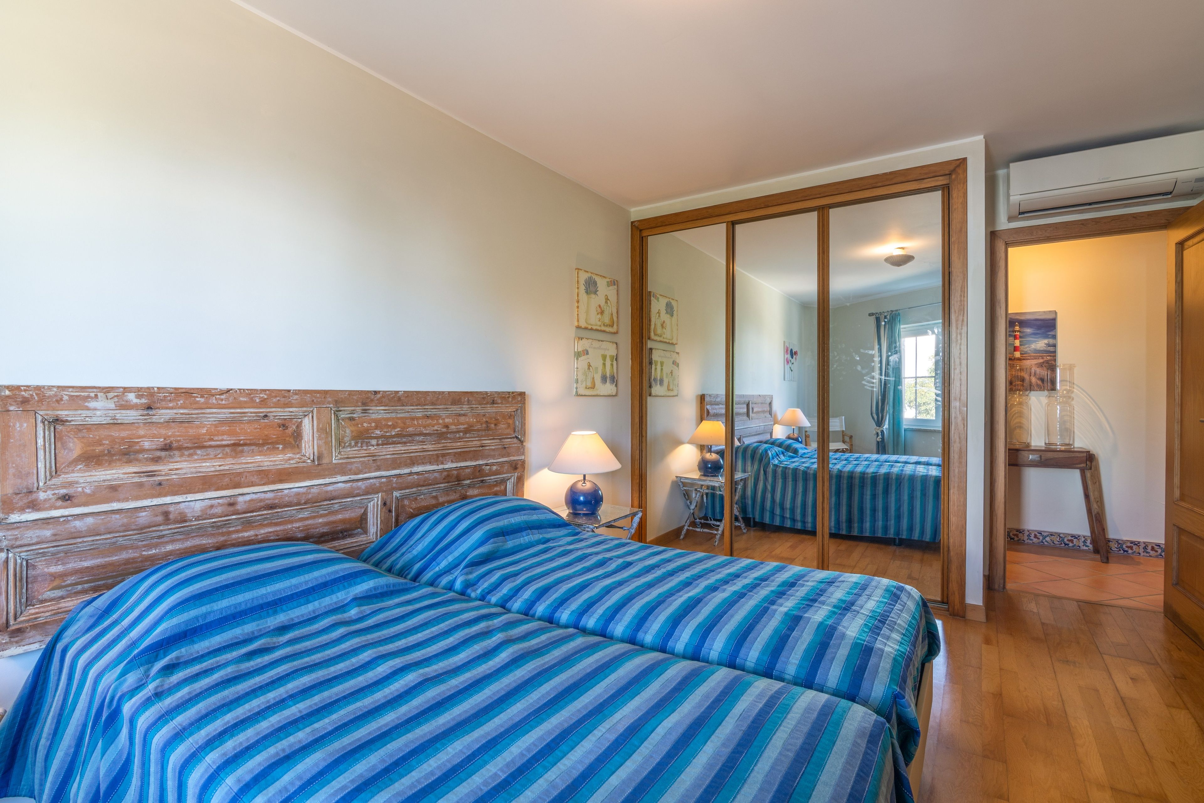 A room with two beds, a wooden headboard, a mirror, and a window with curtains.
