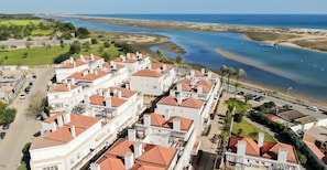 A coastal residential area with white buildings and red roofs, a beach, and a clear view of the sea. - Aldeia Formosa Apartment T2 (Cabanas)