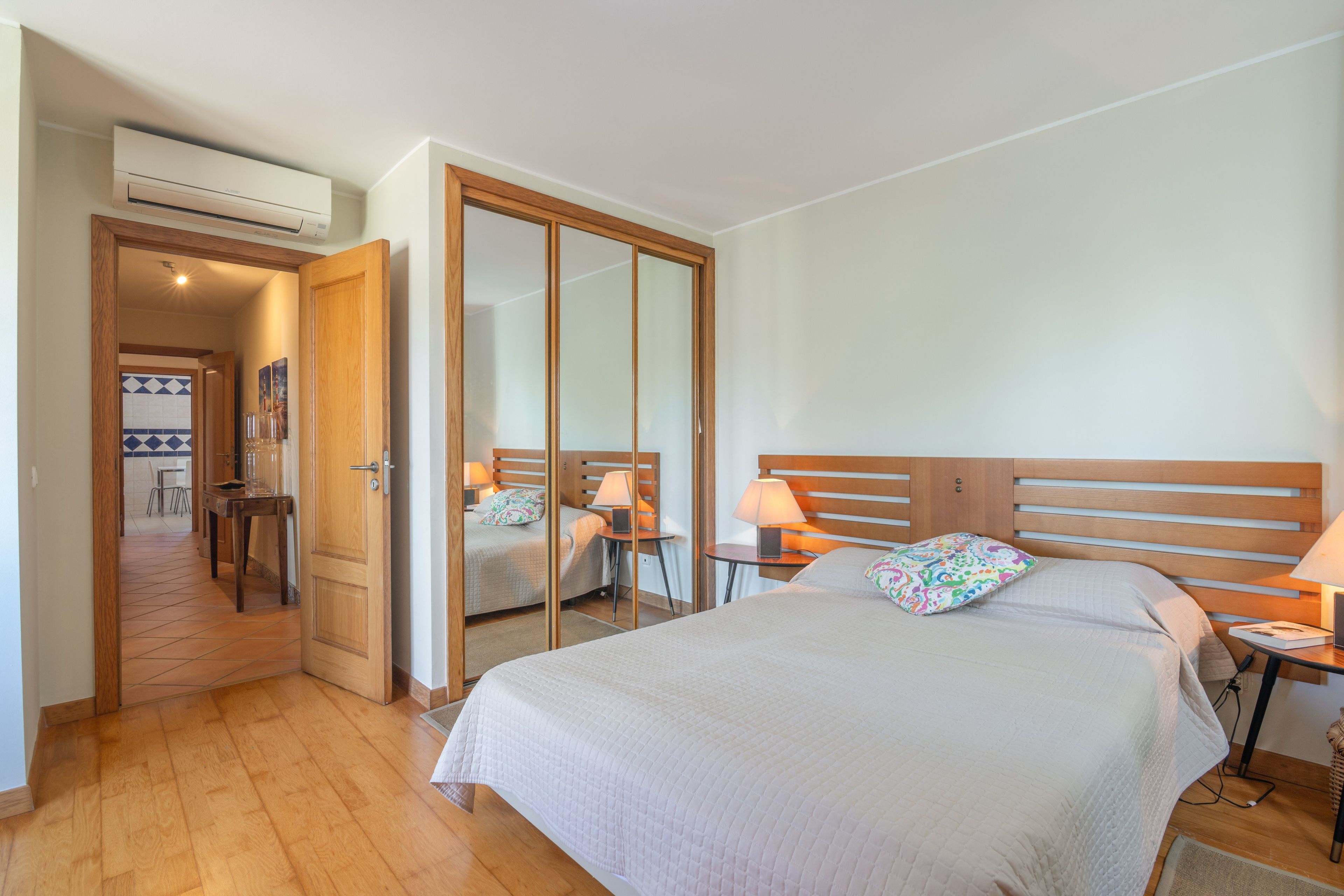 Habitación de hotel con una cama grande, un armario de madera, un escritorio con silla y un equipo de aire acondicionado.