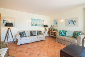 Un salon avec deux canapés, une table basse et un lampadaire. Les murs sont ornés de tableaux et le sol est carrelé.