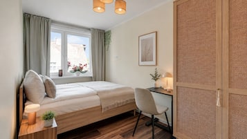 A bedroom with a bed, bedside table, lamp, chair, desk, window, and a door with a woven panel.