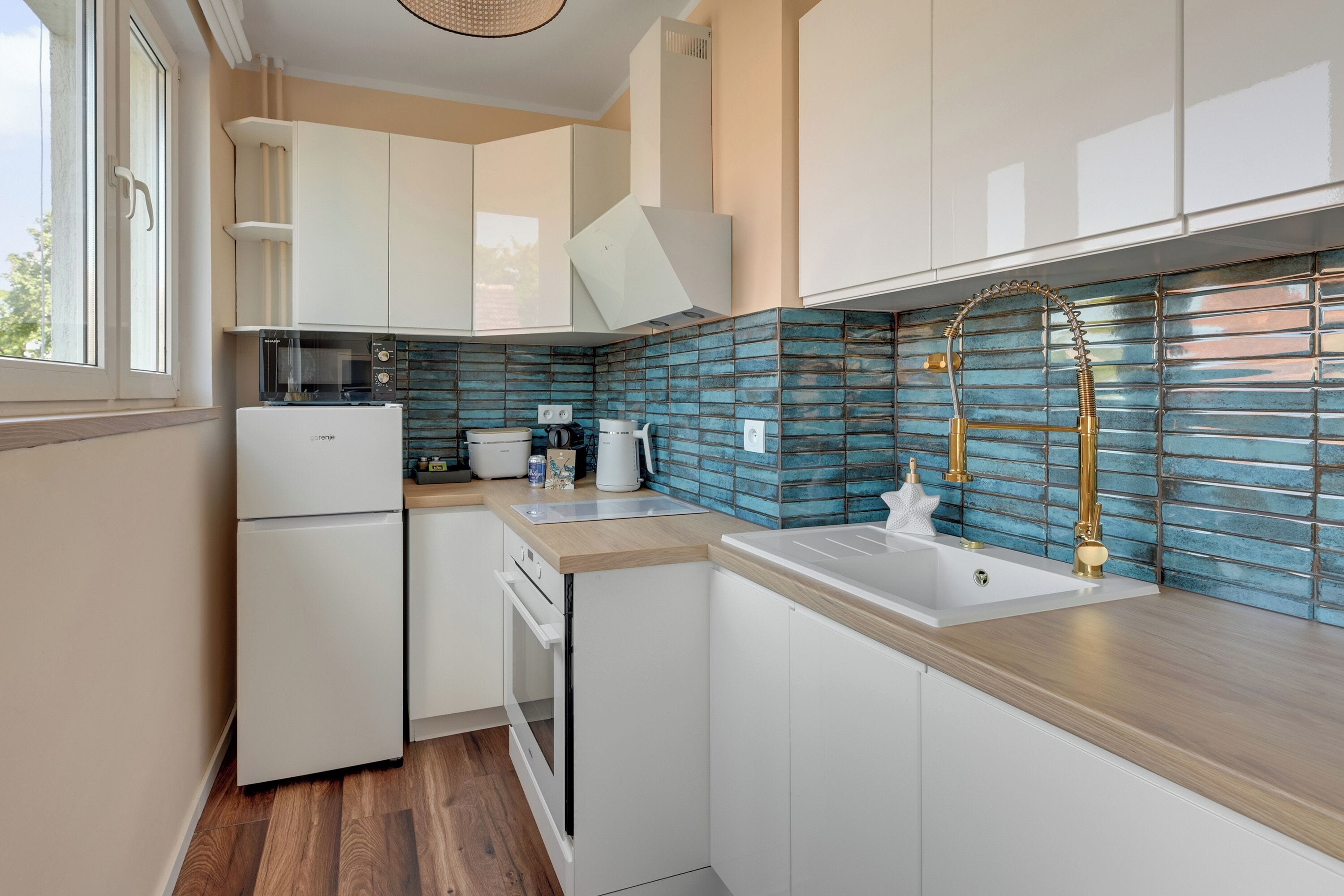 Une cuisine moderne avec des meubles blancs, une cuisinière encastrée et un dosseret de carrelage bleu.