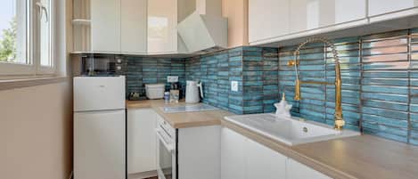 Una cocina moderna con muebles blancos, estufa integrada y salpicadero de azulejos azules.