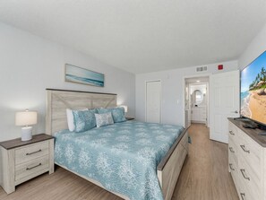 A bedroom with a bed, nightstands, a dresser, a painting, and a television displaying a beach scene. - Walk to Beach + Restaurants - Next to Pool - Grill + Deck -  El Mar "Three Siste (North Redington Beach)