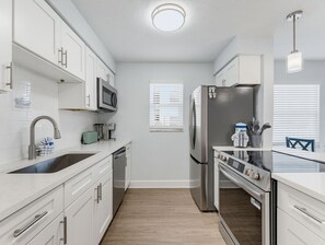 A modern kitchen with white cabinets, stainless steel appliances, a built-in oven, and a window with blinds. - Walk to Beach + Restaurants - Next to Pool - Grill + Deck -  El Mar "Three Siste (North Redington Beach)