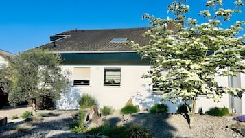Ein zweigeschossiges Gebäude mit einem geneigten Dach, einer Schotterauffahrt und verschiedenen Pflanzen und Sträuchern.