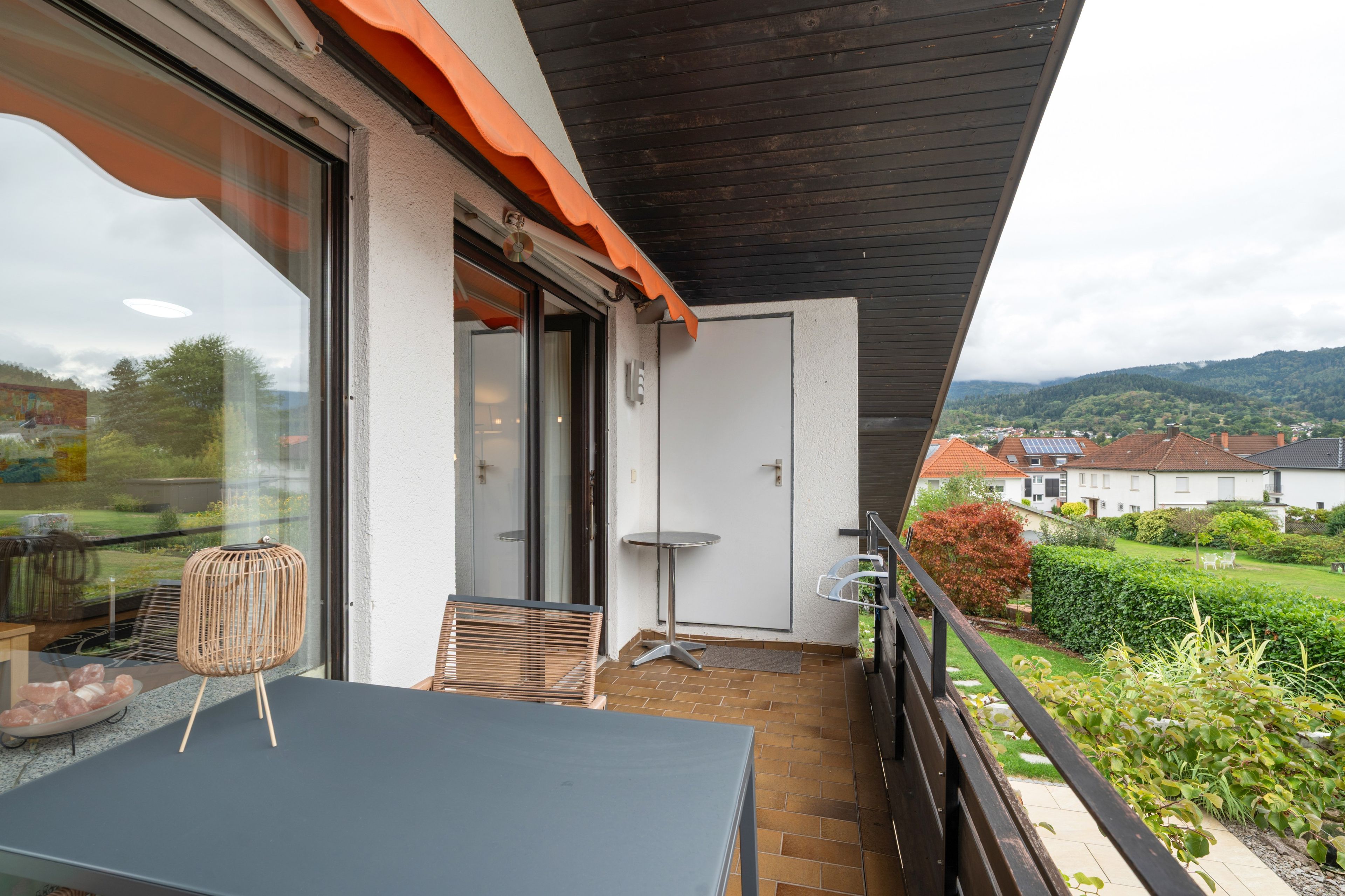 Ein Balkon mit Tisch und Stühlen, einer Tür und Blick auf eine grüne Landschaft mit Häusern.