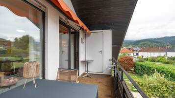 Ein Balkon mit Tisch und Stühlen, einer Tür und Blick auf eine grüne Landschaft mit Häusern.