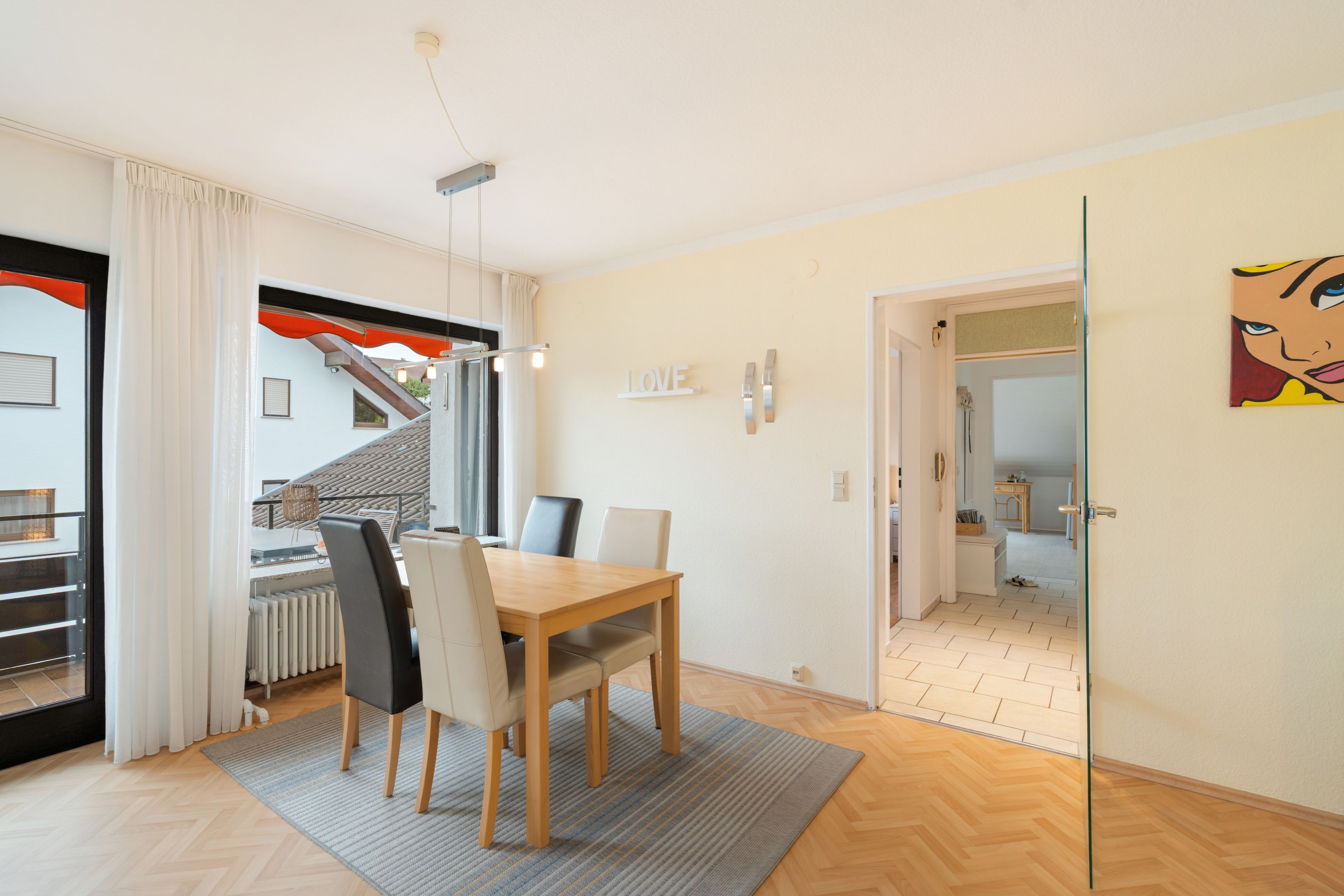 Uma sala de estar moderna com área de jantar, escada e cozinha visível através de uma porta aberta.