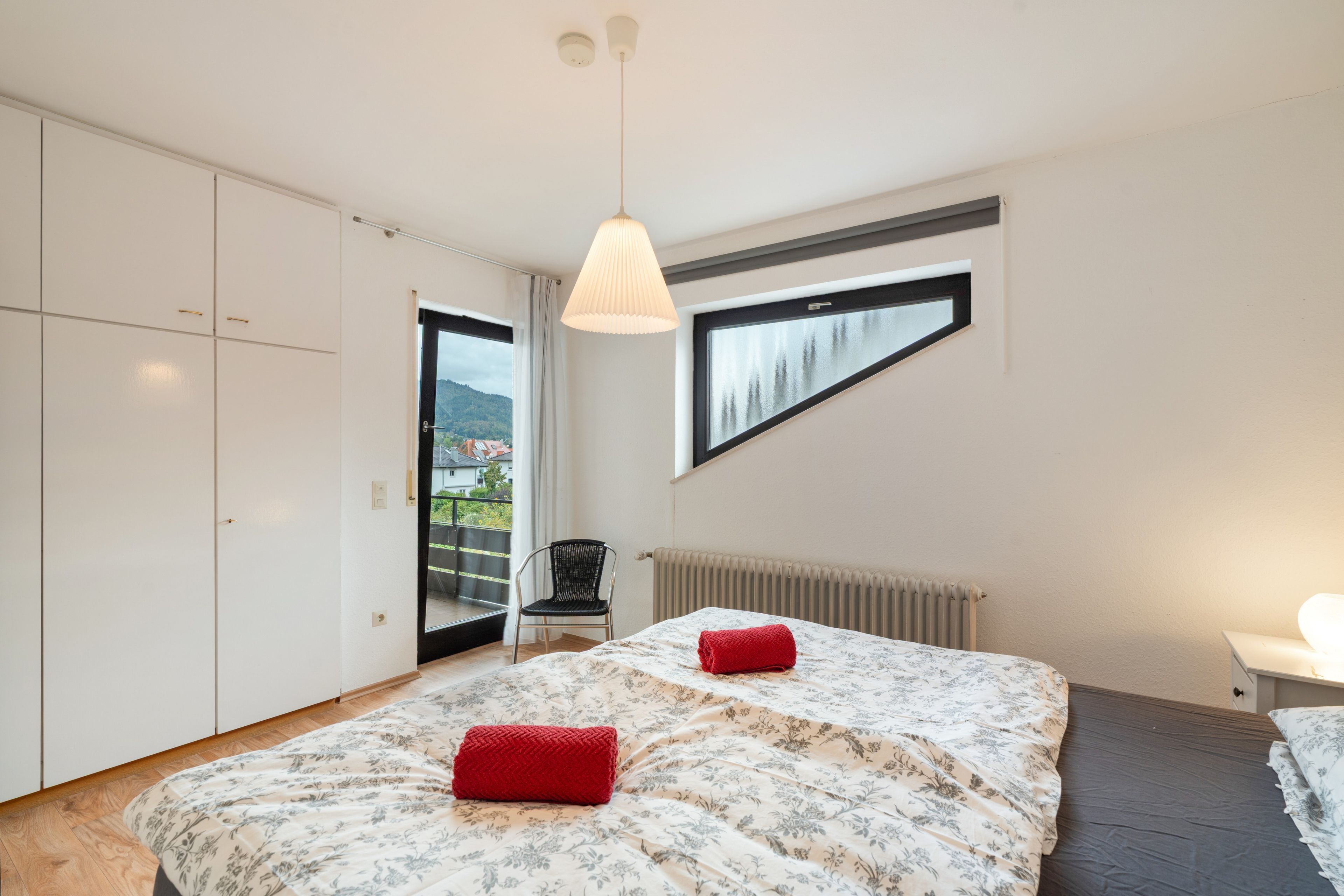A bedroom with a bed, a chair, a radiator, and a window with a view.